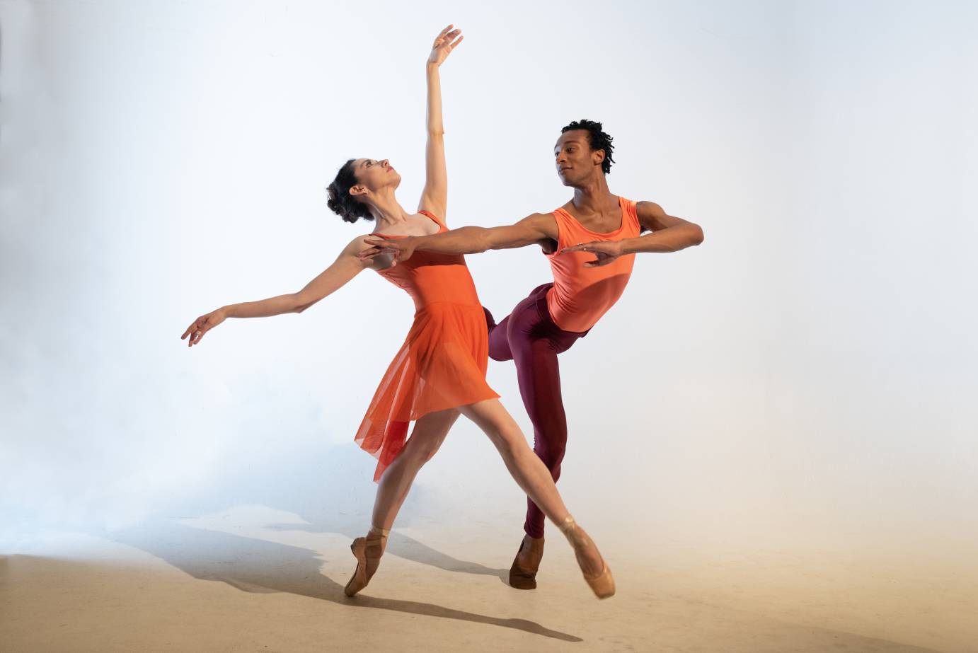 A man and a woman in orange extend into balletic positions